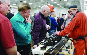 Standing on the right is the author in red with Chris Gergeni, NMLRA managing director, at the working end of the rifling machine talking to a group at Kalamazoo, MI. (Photo by Becky Waterman)